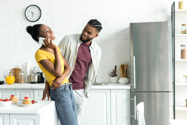 smiling african american boyfriend talking by smartphone at kitchen - Photo, Image