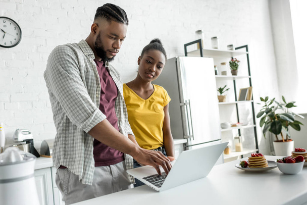 african american couple using laptop together at kitchen - Foto, Bild