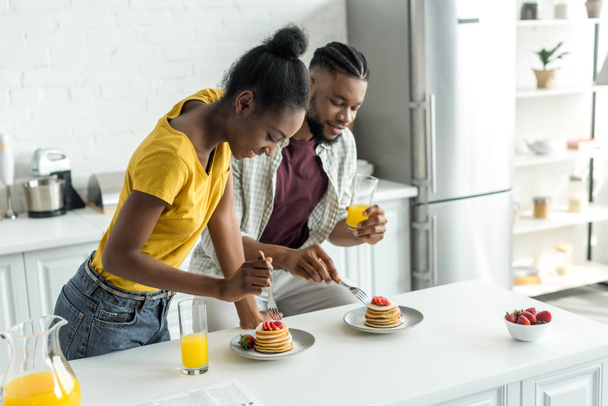 african american couple eating pancakes and drinking orange juice at kitchen - Foto, afbeelding