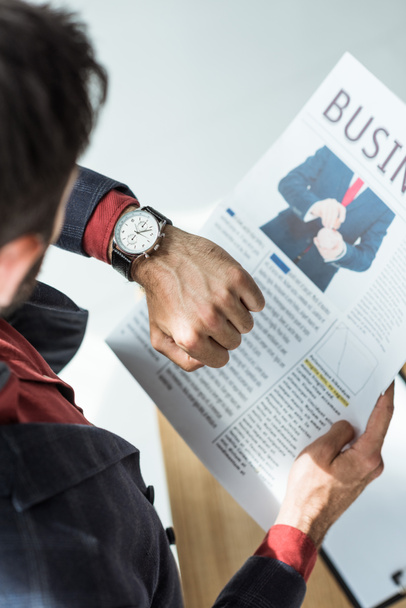 high angle view of businessman reading newspaper and looking at watch at office - Foto, afbeelding