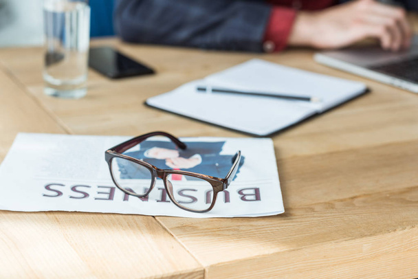 close-up shot of eyeglasses lying on newspaper with blurred businessman working on background - Zdjęcie, obraz