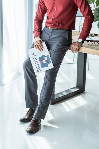 cropped shot of businessman with newspaper leaning back on workplace - Photo, image