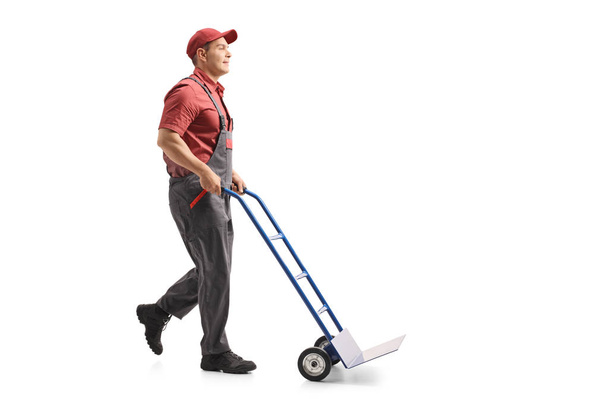 Full length profile shot of a mover pushing an empty hand truck isolated on white background - Foto, Imagem