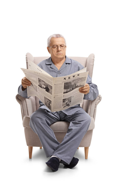Mature man in pajamas sitting in an armchair and reading a newspaper isolated on white background - Photo, Image