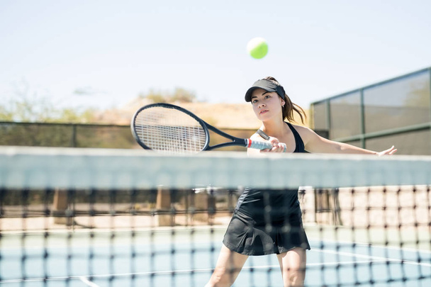 Hyvännäköinen nainen tennispelaaja lyömällä palloa yli verkon kentällä
 - Valokuva, kuva