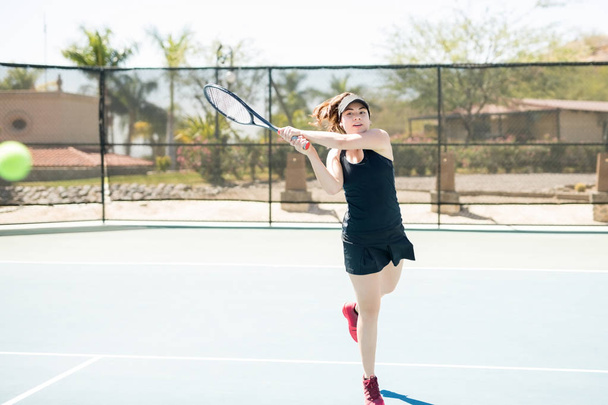 Giocatrice di tennis latina che colpisce la palla con un rovescio, allenandosi duramente per migliorare il suo gioco
. - Foto, immagini