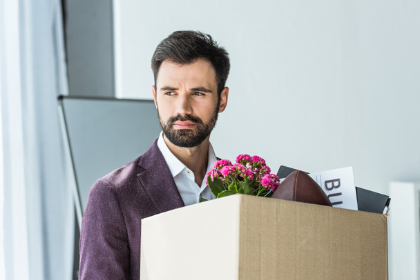 подавленный молодой бизнесмен с коробкой личных вещей после увольнения
 - Фото, изображение