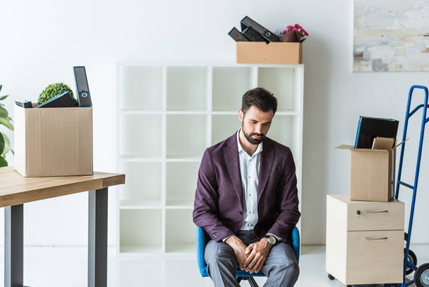 masentunut erotettu liikemies istuu tuolilla toimistossa laatikoiden kanssa henkilökohtaisia tavaroita
 - Valokuva, kuva