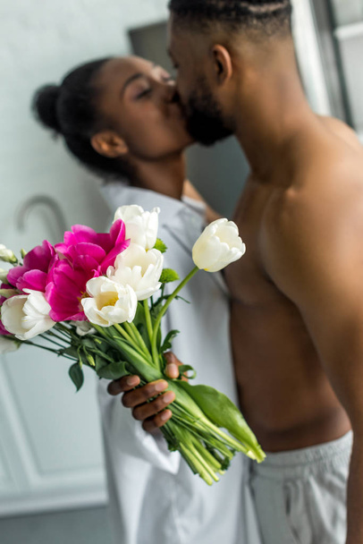 Afrikanisches amerikanisches Paar küsst und Freundin hält Blumenstrauß in der Küche - Foto, Bild
