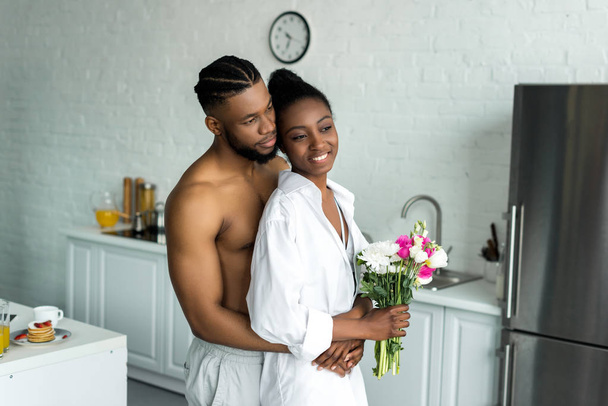 african american boyfriend hugging girlfriend and they looking away at kitchen - Φωτογραφία, εικόνα