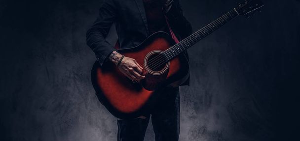 Cropped image of a musician in elegant clothes with a guitar in his hands playing and posing. - Photo, Image