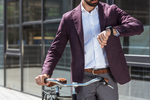 cropped shot of man in stylish suit with vintage bicycle looking at watch - Foto, Bild