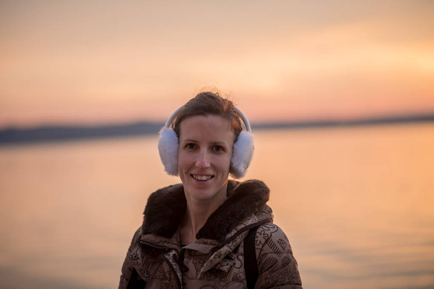 Mujer sonriente con orejeras esponjosas al atardecer
 - Foto, imagen