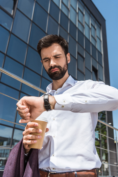 bottom view of handsome young businessman with coffee to go looking at wristwatch - Valokuva, kuva