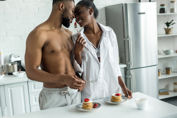 african american girlfriend holding fork with strawberry between her and boyfriend at kitchen - Foto, imagen