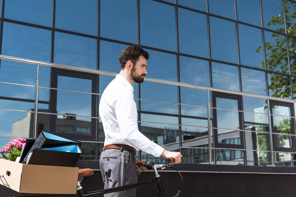 depressed young manager with box of personal stuff on bicycle looking away - Photo, Image