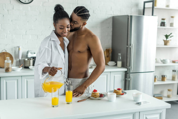 Afrikkalainen amerikkalainen poikaystävä suudella tyttöystävä, kun hän kaataa appelsiinimehua keittiössä
 - Valokuva, kuva