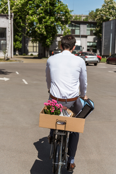 rear view of manager riding on bicycle with box of personal stuff on trunk - Foto, afbeelding