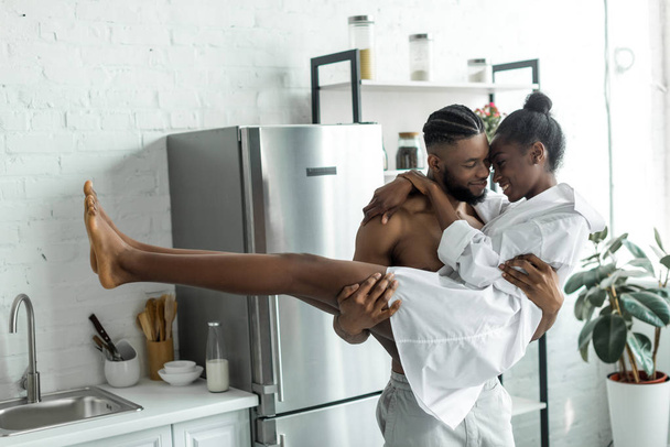 african american boyfriend holding girlfriend at kitchen - Fotó, kép