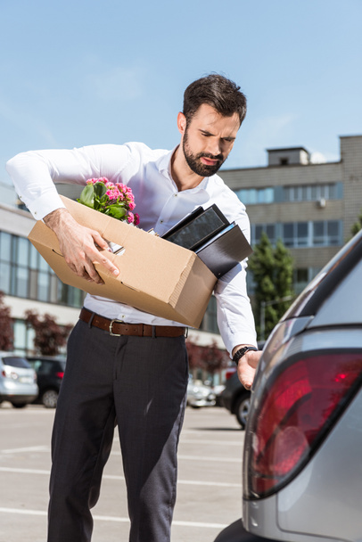 young manager with box of personal stuff opening car trunk on parking - Photo, Image