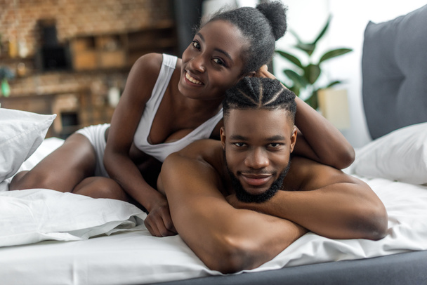 Gelukkig Afrikaanse Amerikaanse echtpaar in ondergoed kijken camera in slaapkamer - Foto, afbeelding