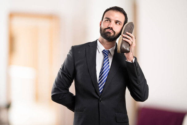Young businessman talking to his shoe over white background - Φωτογραφία, εικόνα