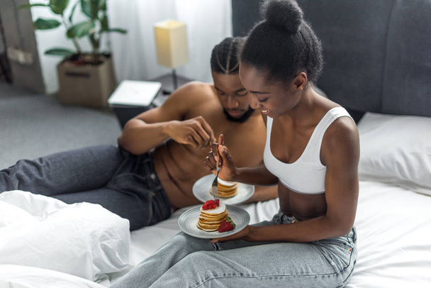 african american couple eating delicious pancakes on breakfast in bedroom - Photo, Image