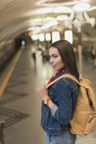 sonriente turista femenina con estilo con mochila en la estación de metro
  - Foto, Imagen