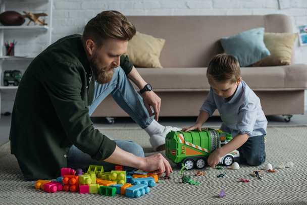 father and little son playing with toy cars together on floor at home - Фото, зображення