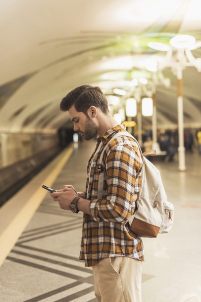 Seitenansicht eines Mannes mit Rucksack und Smartphone an U-Bahn-Station - Foto, Bild