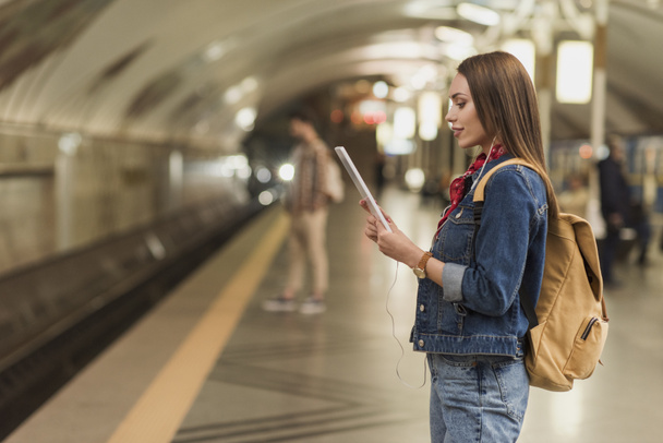 Seitenansicht einer stilvollen Frau mit Kopfhörer und digitalem Tablet an der U-Bahn-Station  - Foto, Bild