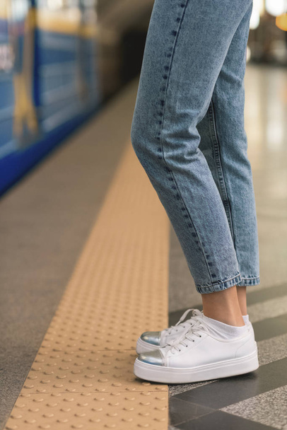 cropped image of female legs in stylish jeans and sneakers at subway station  - Фото, зображення