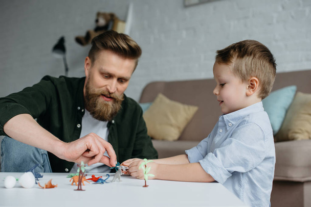father and cute little son playing with various toy dinosaurs together at home - Photo, Image