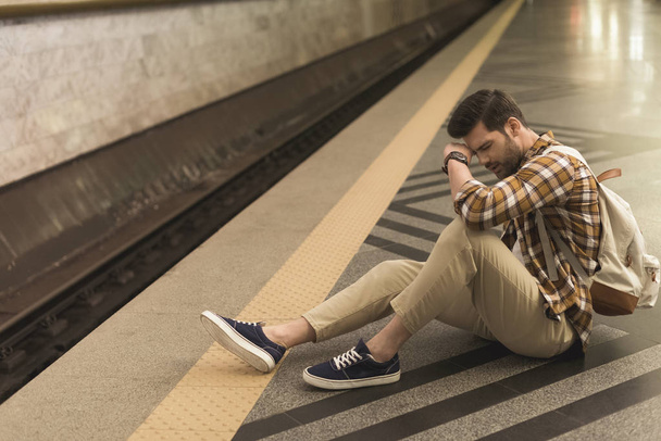 upset young man with backpack late on train and sitting on floor at subway station - Photo, Image