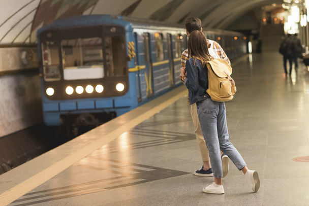 πίσω όψη του κομψό ζευγάρι από ταξιδιώτες με Σακίδια στο σταθμό του μετρό  - Φωτογραφία, εικόνα