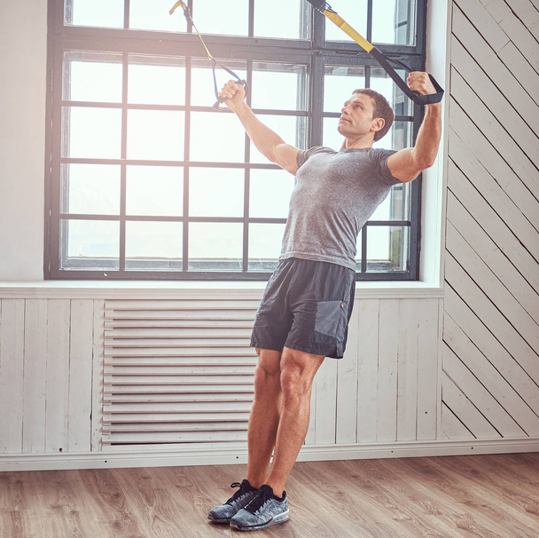 Aptitud muscular masculina haciendo ejercicio con TRX. Entrenamiento funcional en casa con bucles TRX
. - Foto, imagen