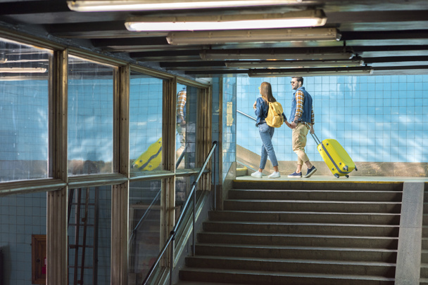 stylish couple with backpack and wheeled bag going upstairs at subway  - 写真・画像