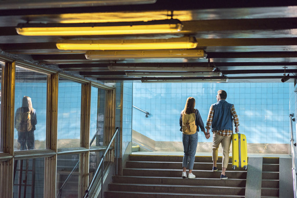 vue arrière du couple élégant avec sac à dos et sac à roulettes allant à l'étage au métro
  - Photo, image