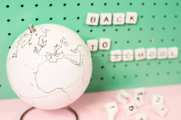 Back to school supplies. White globe and wooden letters on a board, pastel colours - Photo, image