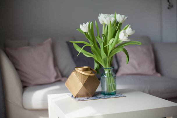 Interior. Room. A bouquet of tulips in a glass vase, a gold candlestick on a white wooden table. Sofa, pillows. Spring. It's cozy. Living room. - Φωτογραφία, εικόνα