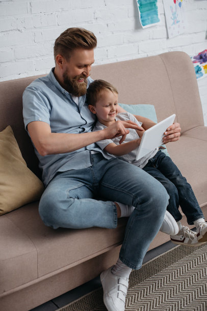 father and little son using tablet together on sofa at home - Valokuva, kuva