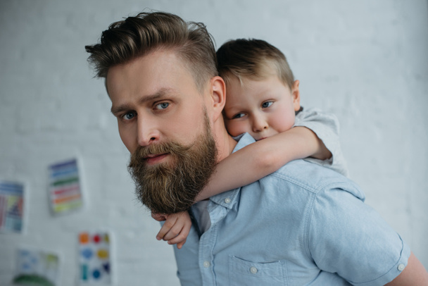 side view of father and son piggybacking together at home - Фото, изображение