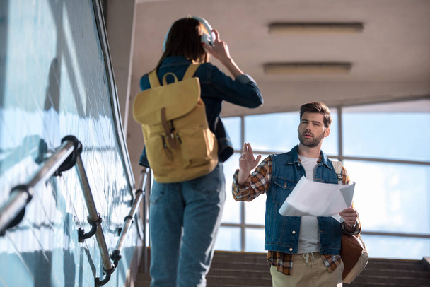 молодий чоловік мандрівник з картою в руці просить допомоги жінці з навушниками та рюкзаком на сходах в метро
 - Фото, зображення