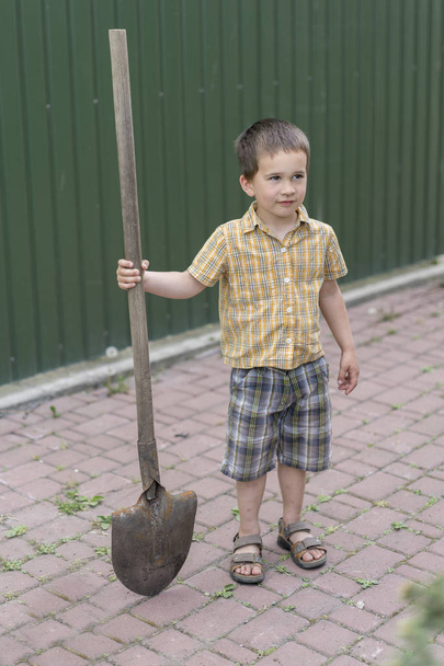 Little boy with a big shovel. little happy boy working with shovel in garden. boy 5 years old keeping a big shovel - Фото, изображение
