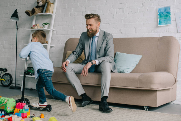 businessman in suit and little son on scooter at home, work and life balance concept - 写真・画像