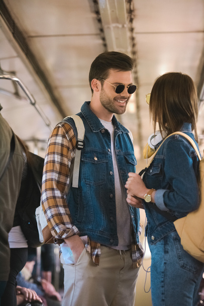 smiling male traveler in sunglasses talking to girlfriend in metro train  - Foto, Imagen
