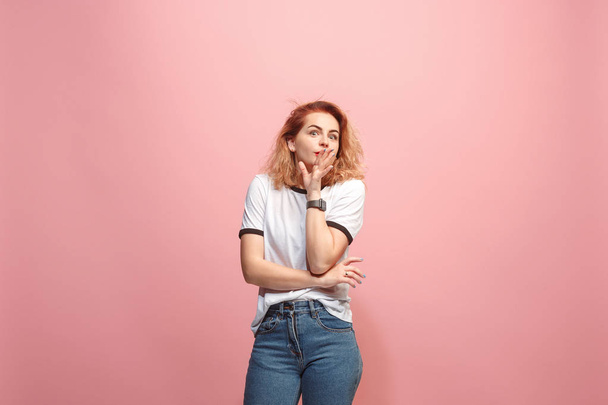 The young woman whispering a secret behind her hand over pink background - Foto, afbeelding