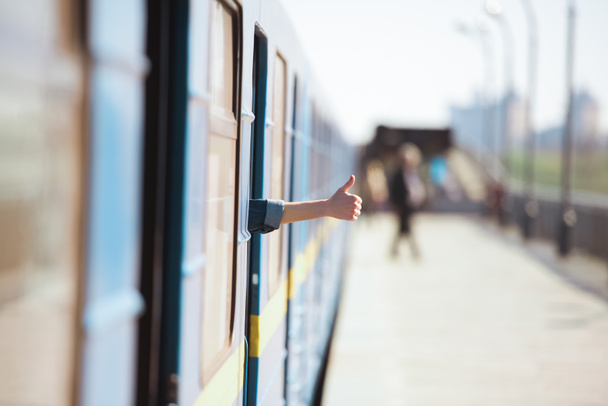 cropped image of female hand looking out from train and doing thumb up gesture at outdoor subway station  - Fotoğraf, Görsel