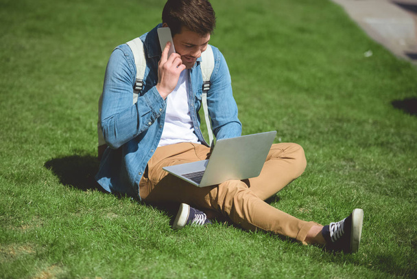 Stilvoller Mann spricht mit Smartphone und Laptop im Gras - Foto, Bild
