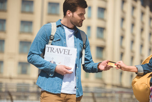 cropped image of female tourist giving credit card to boyfriend with travel newspaper in hand - Photo, Image